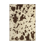 A rectangular area rug with a cow-print pattern featuring dark brown irregular spots on a warm cream background, shown flat against a white background.