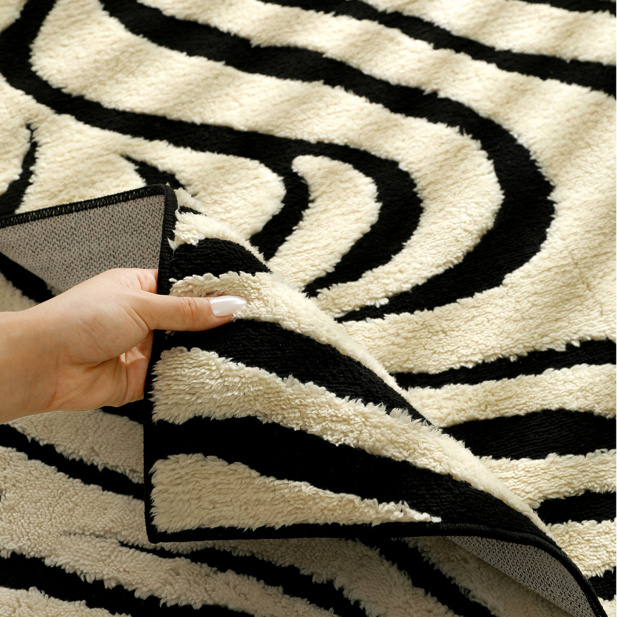 A close-up of a black and cream zebra-patterned rug being held back by a hand to show its plush texture and backing.